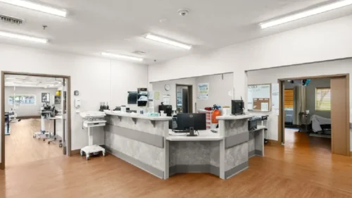 A nurses' station with a curved desk, computers, and medical equipment, with open doorways leading to patient rooms and other areas
