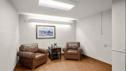 A small sitting room with two brown leather armchairs, a wooden side table, and a framed picture on the wall